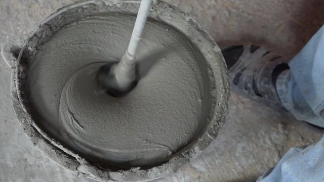 Mixing cement for construction in a small black tank. Worker mixing plaster in a bucket. Worker mixes a solution in a black bucket.