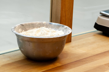 Stainless steel bowl with flour on a wooden table