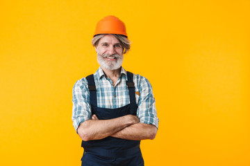 Happy man builder over yellow wall background.