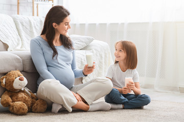 Healthy pregnant mother and little daughter having glass of milk