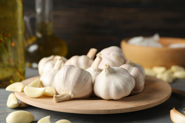 Plate of garlic bulbs, slices, oil on grey table against wooden background, space for text. Closeup