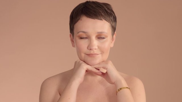 Caucasian woman with short haircut and natural beige makeup in studio on beige background poses to the camera watching to the camera, . Ideal skin natural look