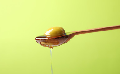 Wooden spoon with olive and pouring olive oil on green background, close up