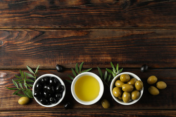 Bowls with olives and oil on wooden background, space for text