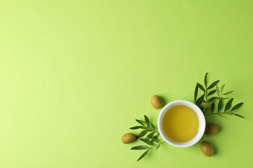Bowl with olive oil, olives and leaves on green background, top view