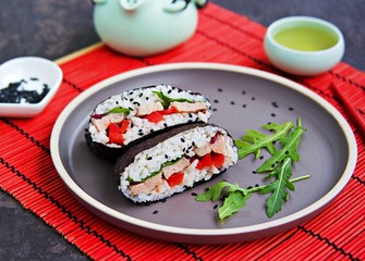 Sushi sandwiches onigirazu with baked duck, spinach and sweet pepper on a brown clay plate on a dark concrete background. Japanese food.