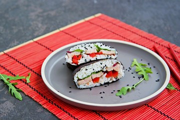 Sushi sandwiches with baked duck, spinach and sweet pepper on a brown clay plate on a dark concrete background. Japanese food.