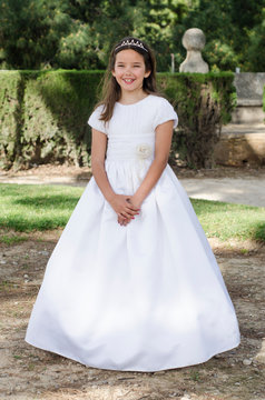 Young girl smiling with crossed hands, ready to take her first communion. White dress of religious communion