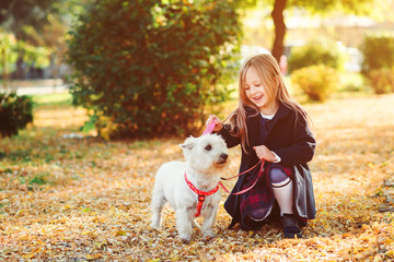 Lovely little girl walking with a dog on a leash in autumn. Best friends, friendship. Happy child with pet in autumn leaves