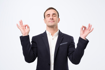 man in suit and white shirt standing, raised arms, closed eyes with yoga gesture and meditation