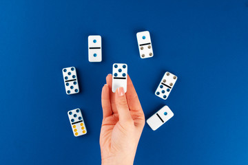 Woman hand holding domino piece  against blue background, top view