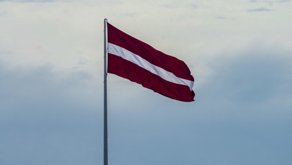 Bordeaux white flag of Latvia against a cloudy sky