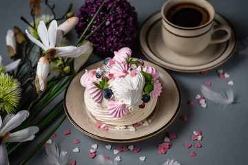 Meringue cake Pavlova with berries and mint leaves. St. Valentine's Day breakfast with flowers and coffee. Beautiful and delicious white and pink cake with hearts made of sugar on grey background