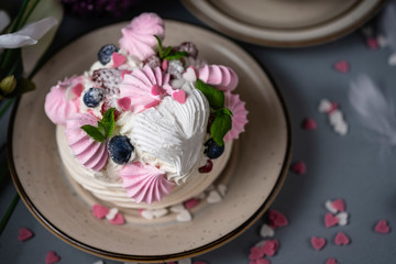Meringue cake Pavlova with berries and mint leaves. St. Valentine's Day breakfast with flowers and coffee. Beautiful and delicious white and pink cake with hearts made of sugar on grey background