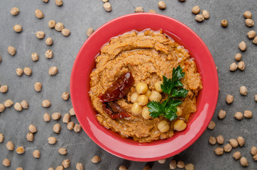 Flat lay view at hummus topped with sun dried tomatoes and green coriander leaves on stone table...