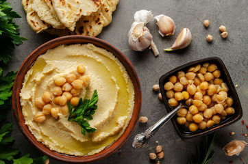 Hummus topped with chickpeas, olive oil and green coriander leaves on stone table with pita bread aside
