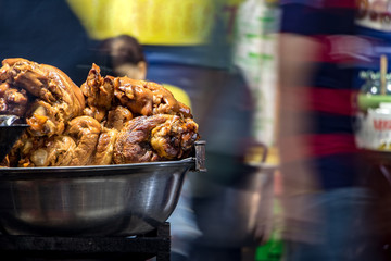 The roasted pieces of meat on pile at a street restaurant, blurred people walking around, Thailand.