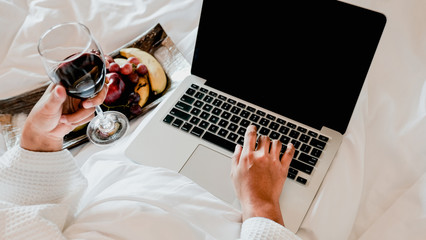 Picture of tourists businesswoman hands work with laptop, holding wine and eating fruits on a bed in the luxury hotel room, healthy food concept.