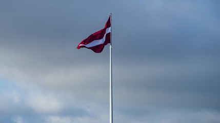 Bordeaux white flag of Latvia against a cloudy sky