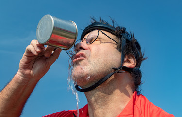 Portrait of a tired cyclist in retro helmet drinks water from cup. Thirsty biker drink beverage...