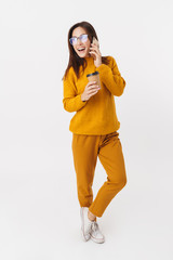 Full length image of adult woman holding coffee and talking on cellphone