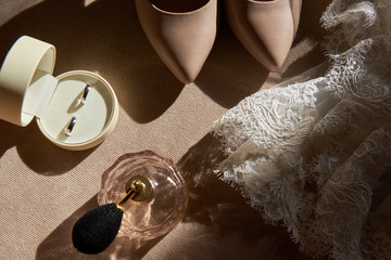 Close up of beige women shoes, two golden wedding rings in box, dress and perfume on chair, copy space. Wedding concept. Top view, flat lay