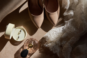 Close up of beige women shoes, two golden wedding rings in box, dress and perfume on chair, copy...