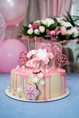 Round pink birthday cake decorated with lollipops, gingerbreads, flowers, beads number two on the top, copy space. Cake and ballons on blue table