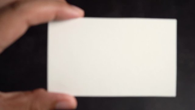 Hand holding mockup white business card on black background, Zoom out slow motion.
