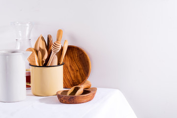 Wooden set of kitchenware in iron cup with wooden plates on white textile table. Cooking appliances. Zero waste