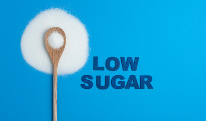 Composition with sugar, written word LOW SUGAR, wooden spoon with sugar, on blue background, top view