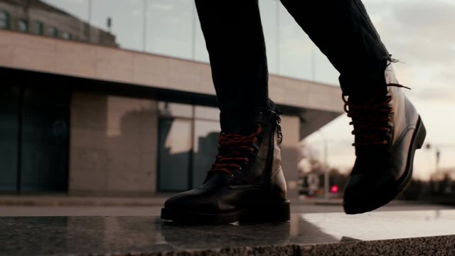 Close up view of woman fashion leather black boots walking posing in the evening street. Fashion footwear.