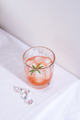 Pink cocktail with rosemary and ice in glass on a white tablecloth on the table