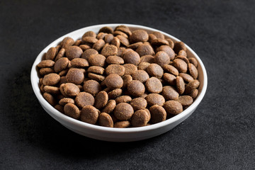 Dry pet food in a white ceramic bowl on black background