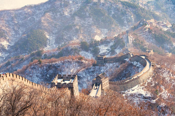 The great wall china in the winter time with snow on the mountain.