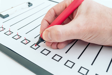 close-up of hand holding red pen ticking off checklist or to-do list on clipboard