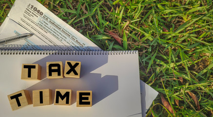 Tax-filling concept - Tax time words on wooden blocks with the U.S IRS 1040 form and pen in nature background