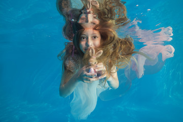 Obraz na płótnie Canvas Young beautiful girl in a white dress posing underwater in the pool
