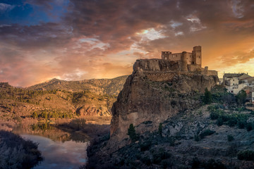 Fototapeta premium Aerial panoramic view of medieval partially restored Cofrentes castle above the Cabriel river in Spain with reflection and dramatic sky
