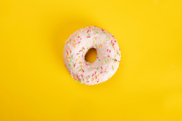 Glazed donut with colorful sprinkles on yellow background. Sweet pastries for Fat Thursday.