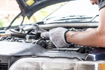 Hand of car mechanic or technician holding wrenches near car open hood. Car service concept.