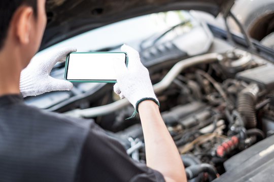 Hand of car mechanic or technician holding smartphone taking photography of car engine open hood. Car service concept.