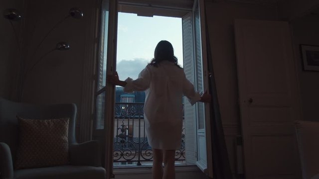Young woman in a white shirt opening the door to the balcony 