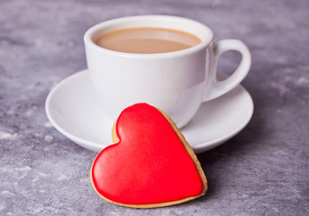 Cup of coffee and a heart shaped red cookie on the gray table
