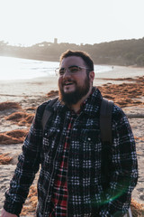 young man smiling on the beach with glasses and beard at sunset