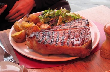 A plate of traditional Florentine steak, potatoes, and salad greens at a restaurant in Florence, Italy 