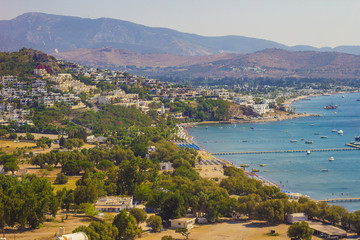 Fototapeta premium Beautiful panoramic view on Bodrum marina. Turkish beach vacation on the shores of Aegean sea. Stylish white buildings, green trees on foreground. Bodrum city, Mugla, Turkey. Soft focus