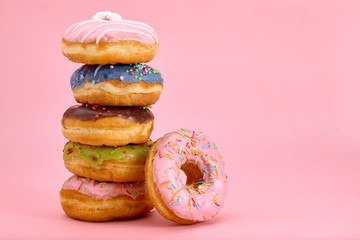 Sweet donuts stacked in a stack on a pink background. Copy space, game of color, sweet life.