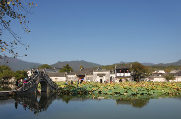 Fototapeta na wymiar Hongcun Ancient Town in Anhui Province, China. View of the stone bridge crossing Nanhu Lake in Hongcun. Ancient town of Hongcun in China with bridge, old buildings and lilies.