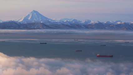 Obraz na płótnie Canvas In Kamchatka early in the morning at dawn in the fog ships are in the Pacific ocean on the background of a volcano